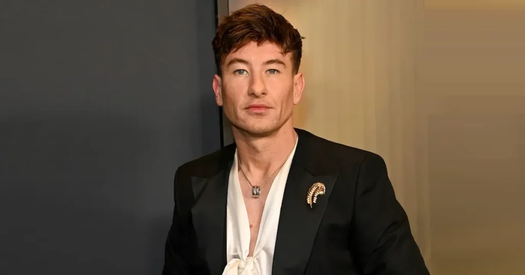 Barry Keoghan smiling in a black suit at a red carpet event.
