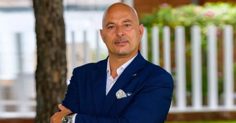 Gianluca Cugnetto smiling in a blue jacket outdoors with green leaves in the background